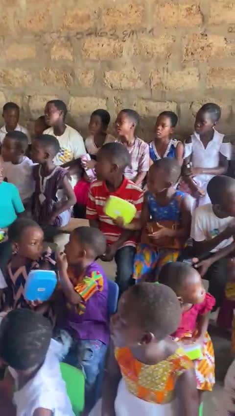 Children in a community classroom holding lunch boxes